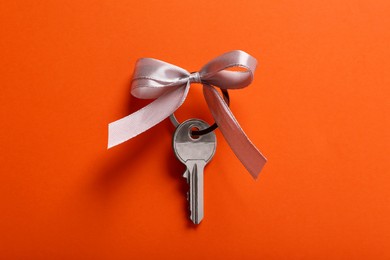 Photo of Key with grey bow on orange background, top view. Housewarming party