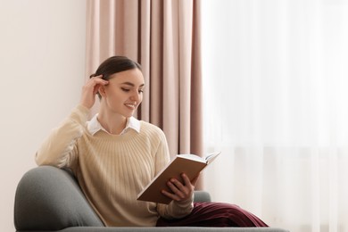 Photo of Woman reading book on sofa near window at home. Space for text