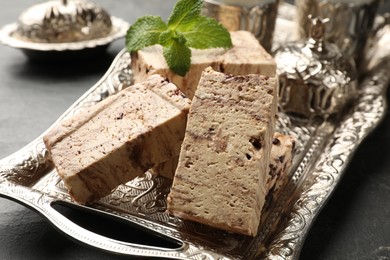 Photo of Tasty chocolate halva and mint on black table, closeup