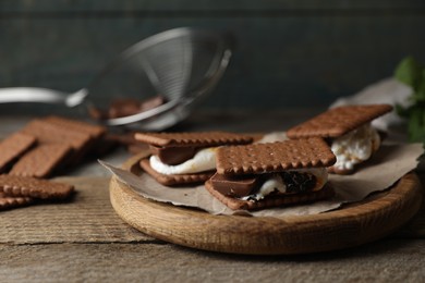 Delicious marshmallow sandwiches with crackers and chocolate on wooden table, closeup