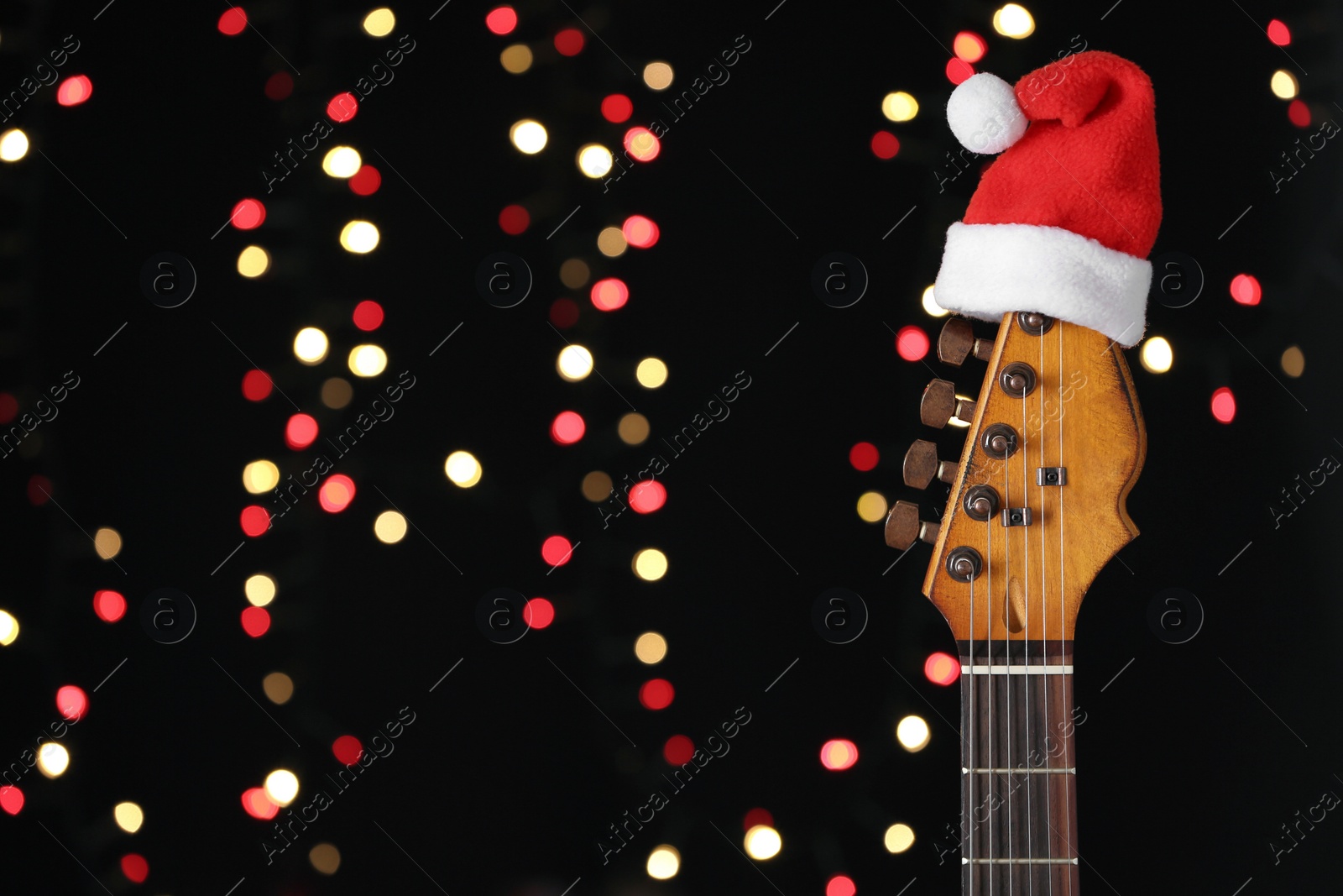 Photo of Guitar with Santa hat against blurred lights, space for text. Christmas music