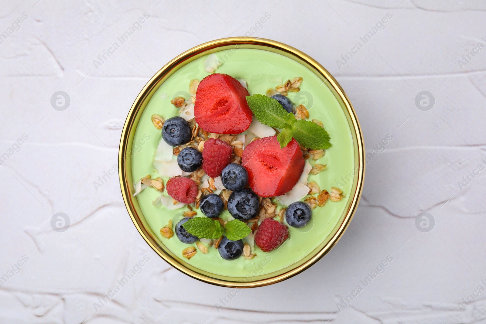 Photo of Tasty matcha smoothie bowl served with berries and oatmeal on white textured table, top view. Healthy breakfast