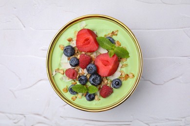 Tasty matcha smoothie bowl served with berries and oatmeal on white textured table, top view. Healthy breakfast