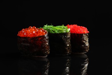 Photo of Delicious sushi with red caviar and seaweed salad on black background