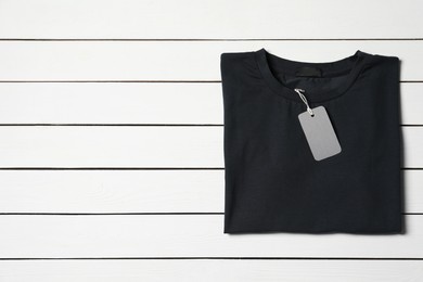 Photo of Stylish black T-shirt with label on white wooden table, top view. Space for text