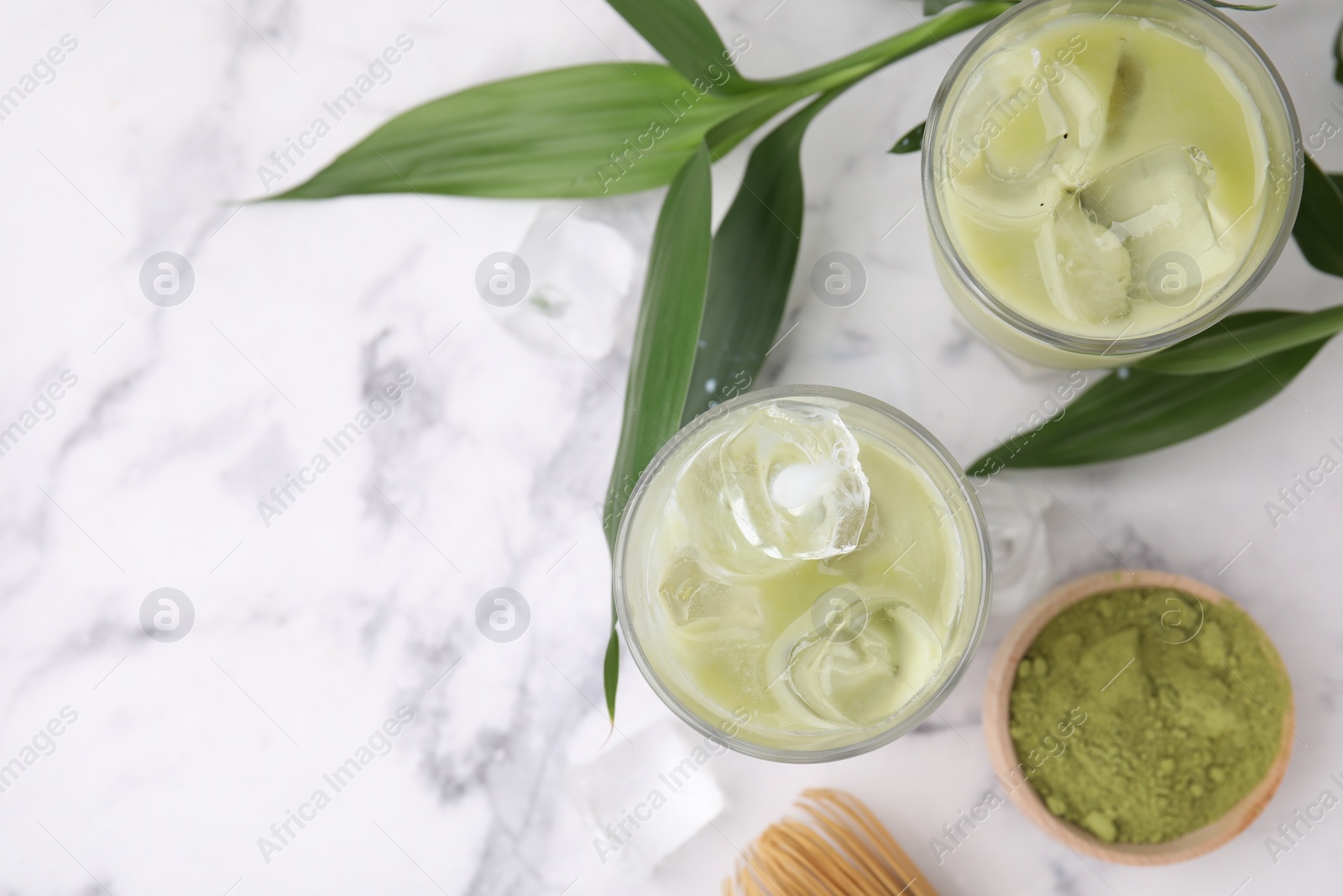 Photo of Glasses of tasty iced matcha latte, powder and leaves on white marble table, flat lay. Space for text