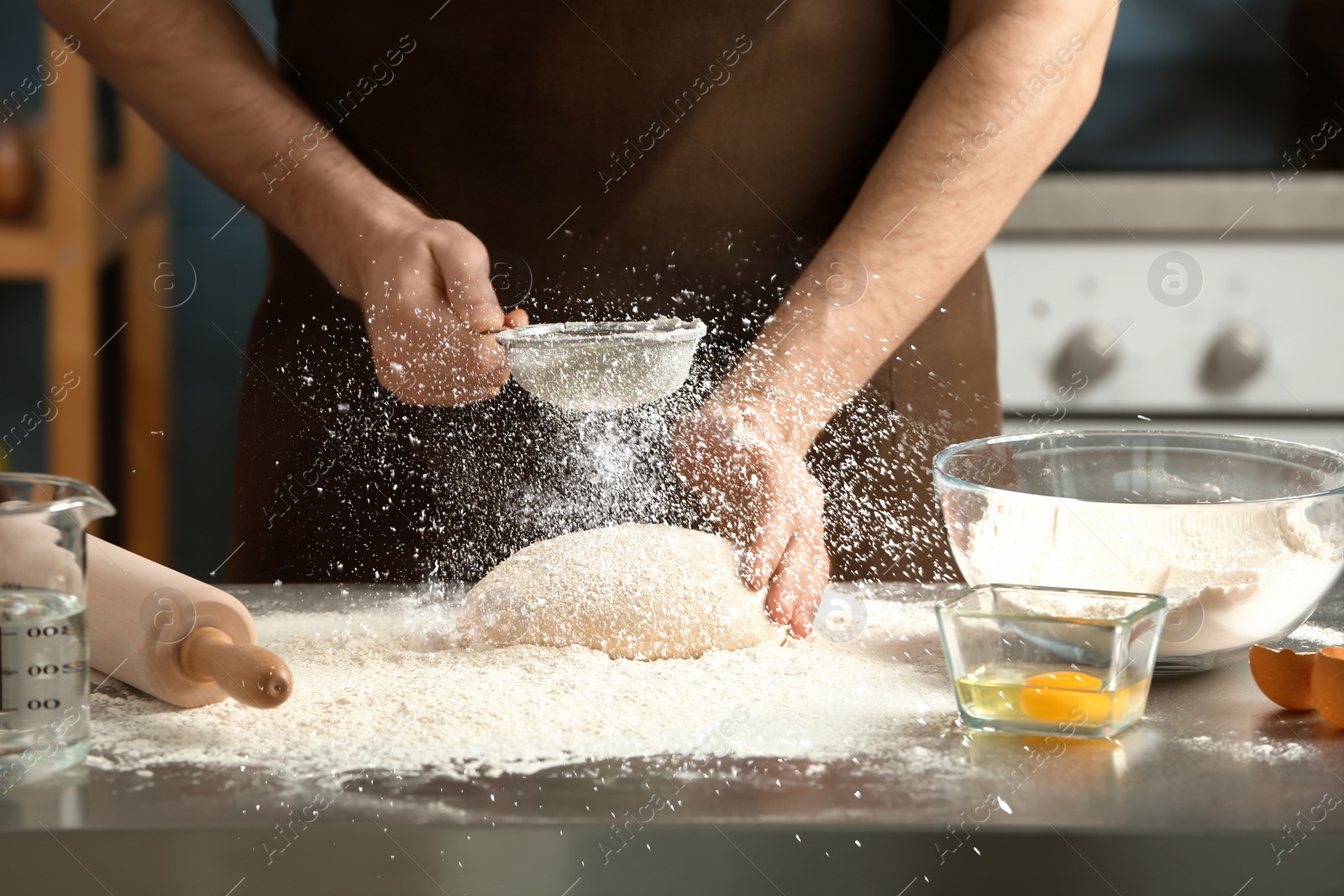 Image of Man sprinkling flour over dough on table in kitchen, closeup