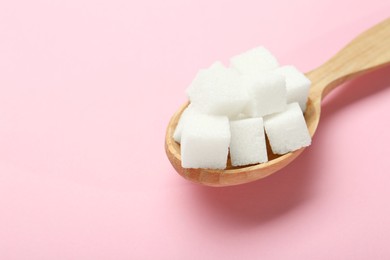 Photo of White sugar cubes in wooden spoon on pink background, closeup. Space for text