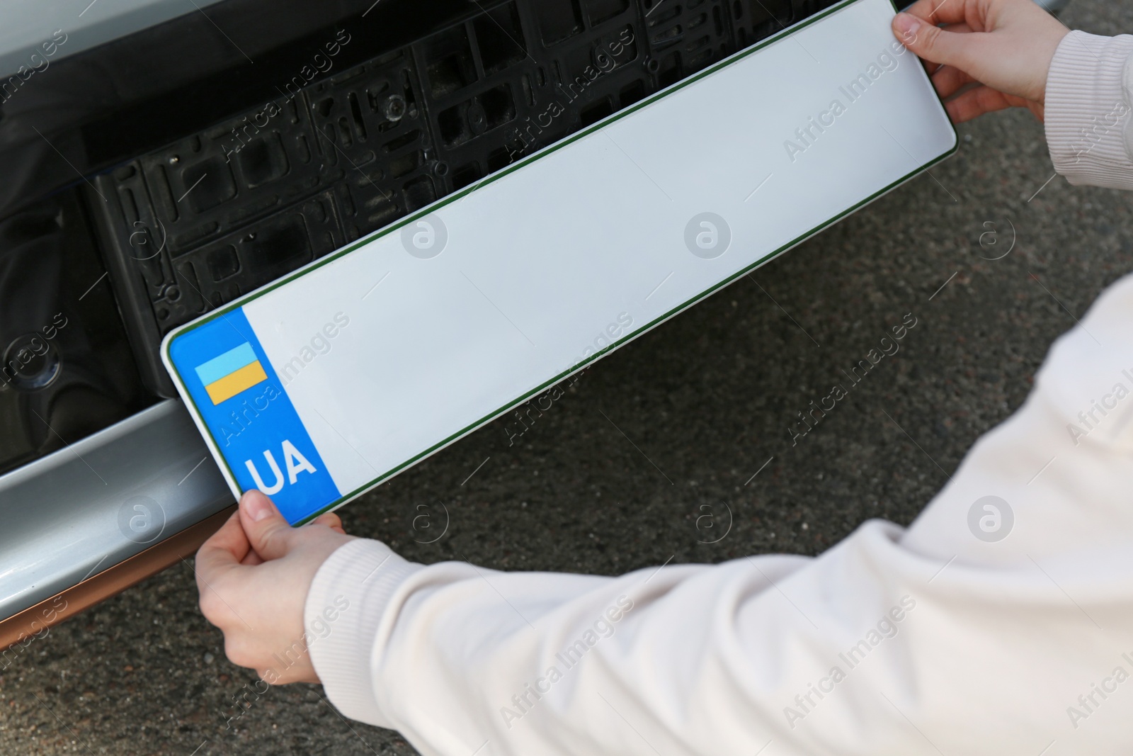 Photo of Woman installing vehicle registration plate outdoors, closeup