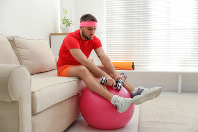 Photo of Lazy young man with sport equipment on sofa at home