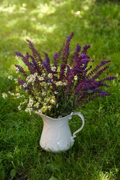 Photo of Beautiful bouquet with field flowers in jug on green grass