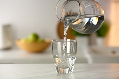 Photo of Pouring water from jug into glass on white marble table in kitchen