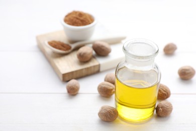 Photo of Bottle of nutmeg oil and nuts on white wooden table, closeup. Space for text