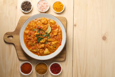 Delicious chicken curry and spices on wooden table, flat lay. Space for text