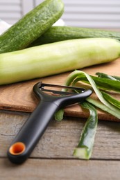 Photo of Fresh cucumbers, peels and peeler at wooden table