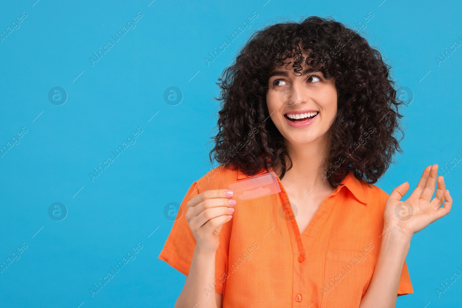 Photo of Young woman holding teeth whitening strips on light blue background, space for text