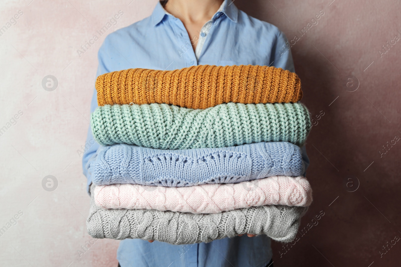 Photo of Woman holding stack of warm clothes on light background, closeup. Autumn season