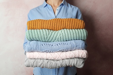 Photo of Woman holding stack of warm clothes on light background, closeup. Autumn season