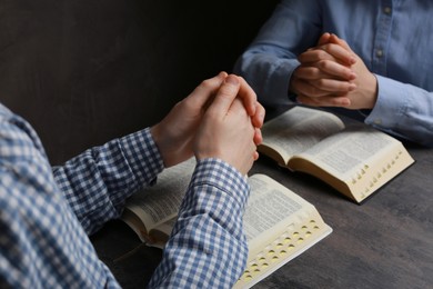 Couple praying over Bibles at grey table, closeup
