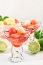 Photo of Glass of melon and watermelon ball cocktail on white wooden table