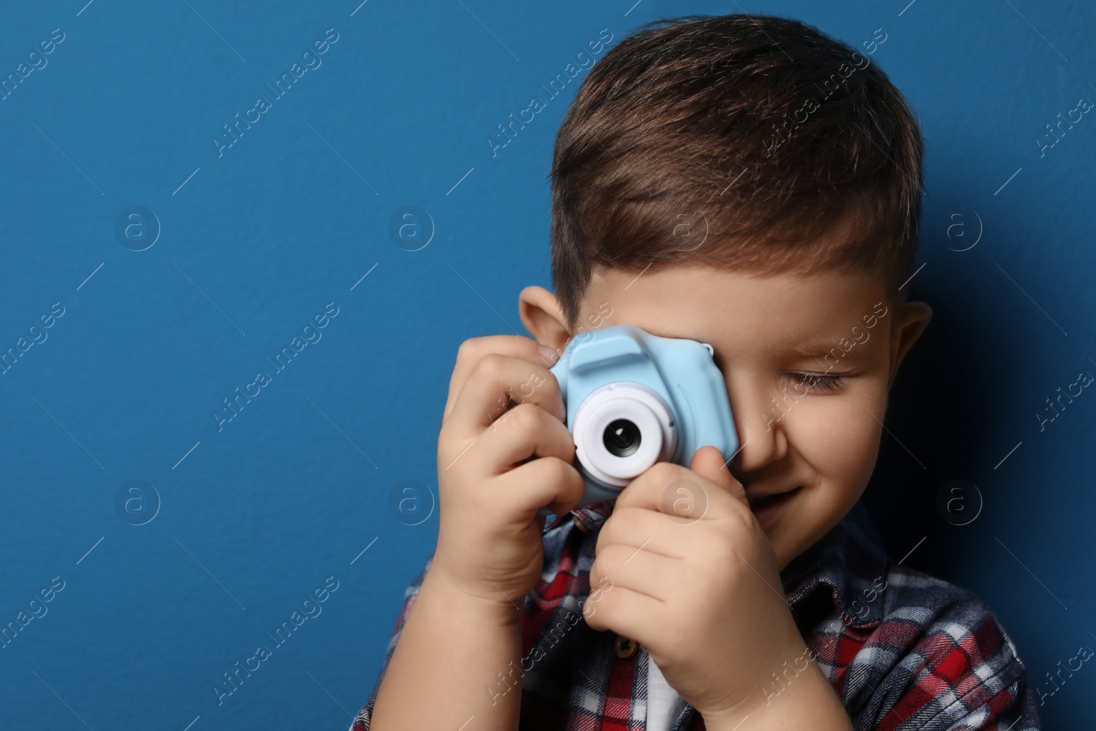 Photo of Little photographer taking picture with toy camera on blue background