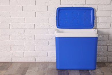 Photo of Open blue plastic cool box near white brick wall. Space for text