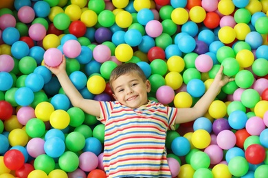 Photo of Cute little child playing in ball pit at indoor amusement park