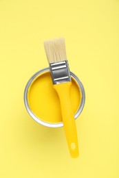 Can of paint with brush on pale yellow background, top view