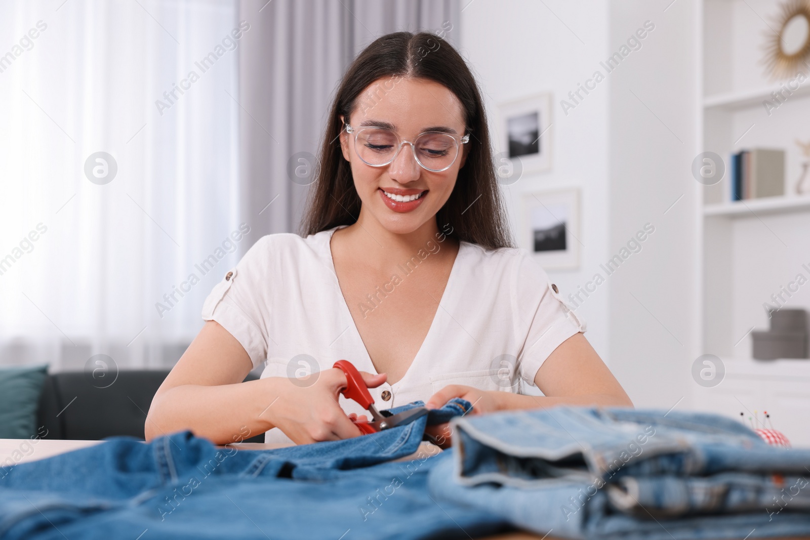 Photo of Happy woman cutting hem of jeans at table indoors