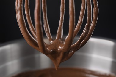 Photo of Chocolate cream flowing from whisk into bowl on black background, closeup