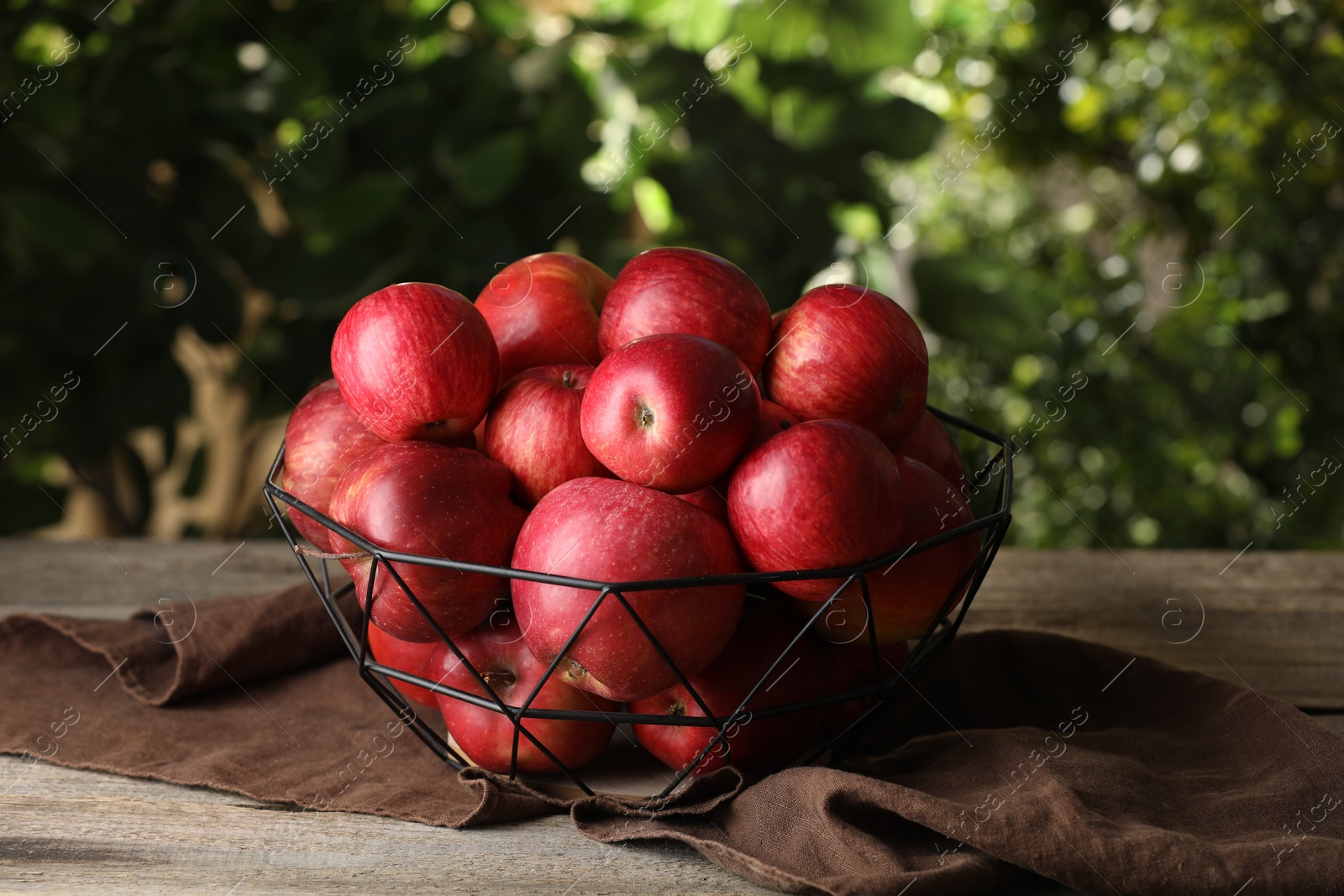 Photo of Ripe red apples in bowl on wooden table outdoors