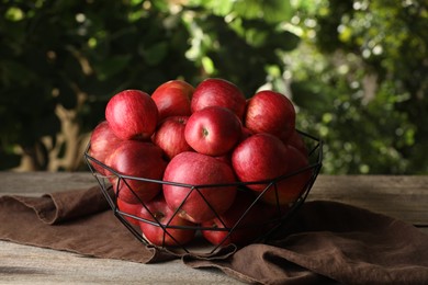 Photo of Ripe red apples in bowl on wooden table outdoors