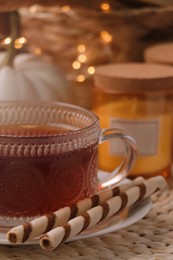 Photo of Cup of hot drink with cookies on wicker mat indoors