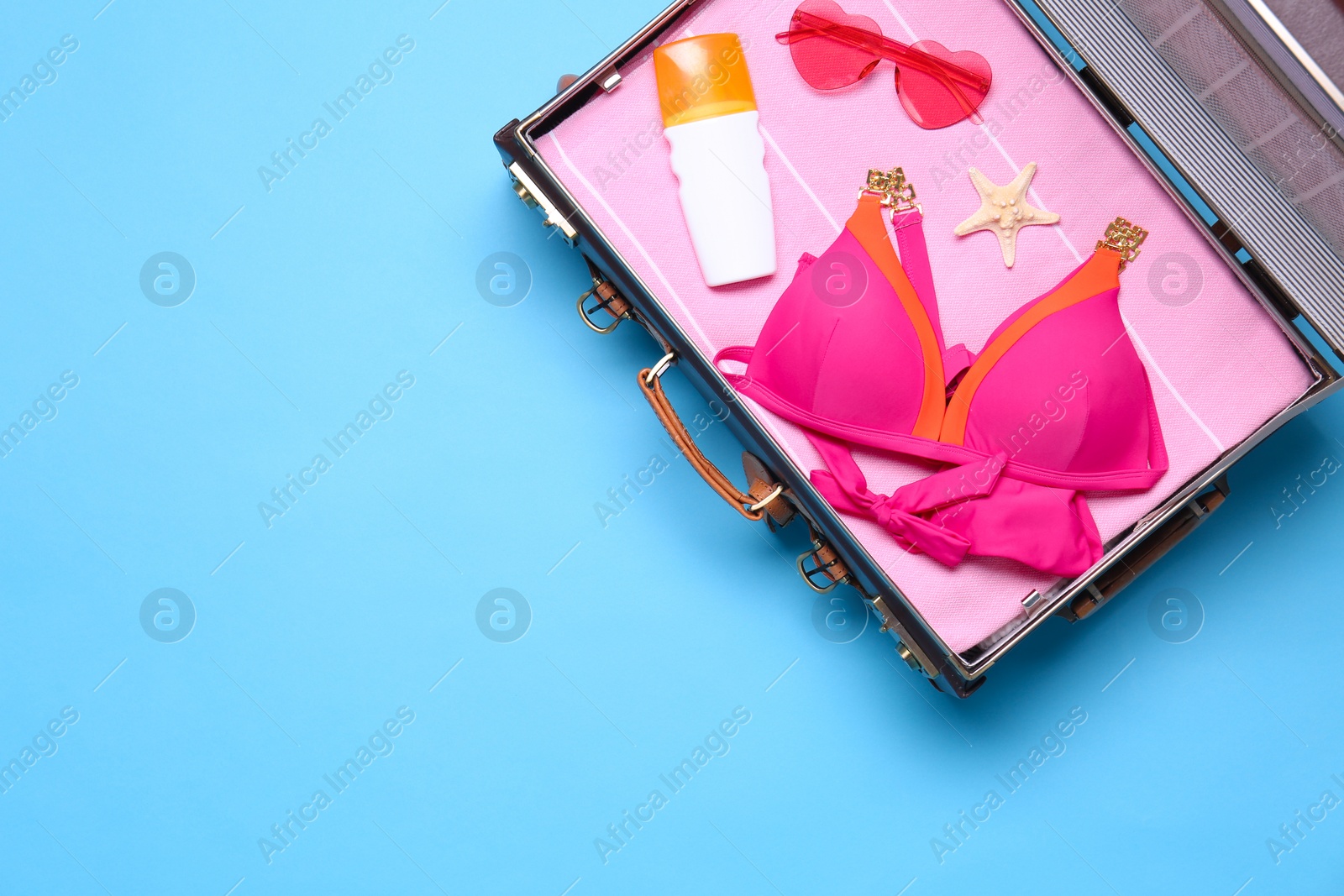 Photo of Open vintage suitcase with beach objects on blue background, top view. Space for text