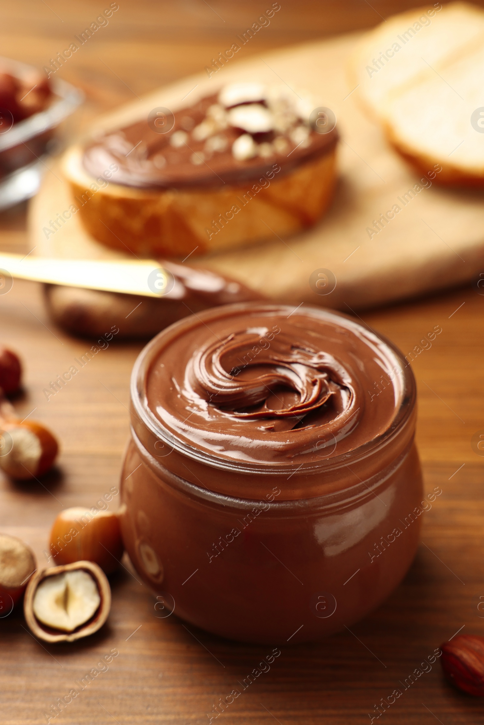 Photo of Glass jar with tasty chocolate hazelnut spread and nuts on wooden table