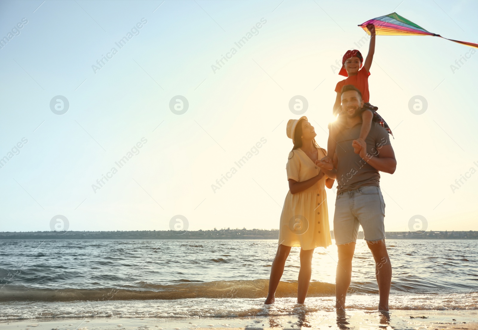 Photo of Happy parents and their child playing with kite on beach near sea. Spending time in nature