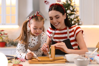 Photo of Mother and daughter making gingerbread house at table indoors