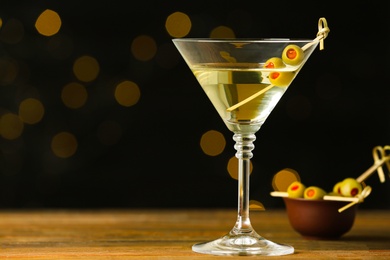 Photo of Glass of Classic Dry Martini with olives on wooden table against blurred background. Space for text