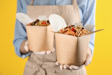 Photo of Chef holding boxes of wok noodles with seafood on yellow background, closeup