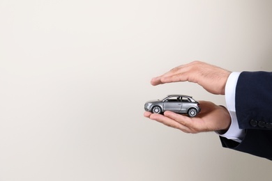 Photo of Male insurance agent holding toy car on light background, closeup. Space for text
