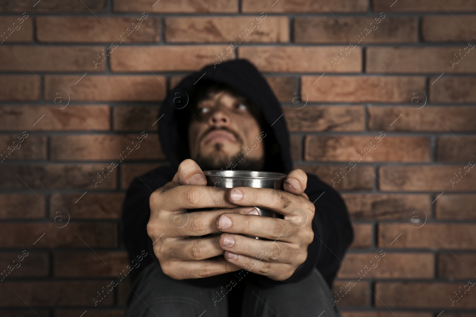 Photo of Poor homeless man begging near brick wall