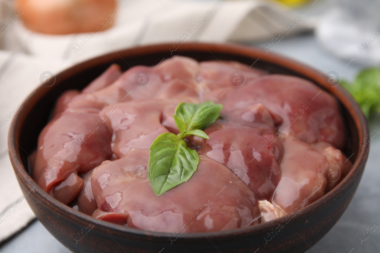 Photo of Bowl with raw chicken liver and basil on table, closeup