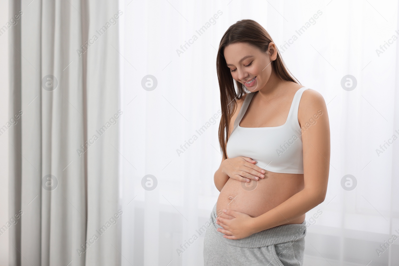 Photo of Beautiful pregnant woman near window indoors, space for text