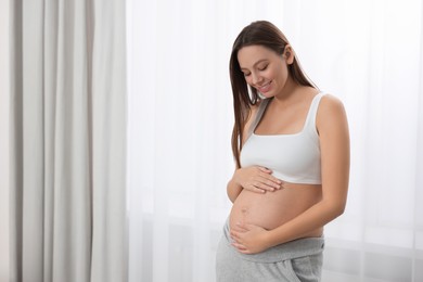 Beautiful pregnant woman near window indoors, space for text