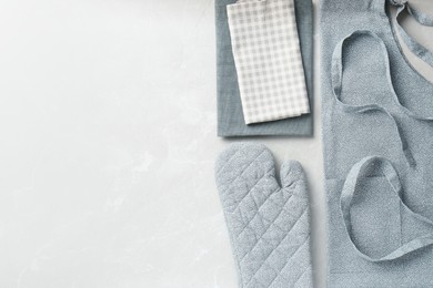 Photo of Kitchen napkins, apron and glove on light marble table, flat lay. Space for text
