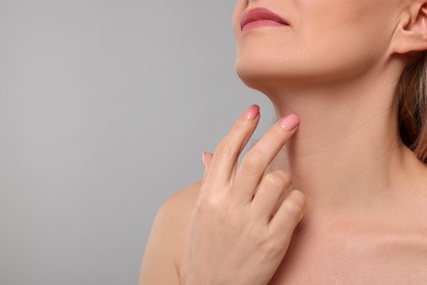 Photo of Woman touching her neck on grey background, closeup. Space for text