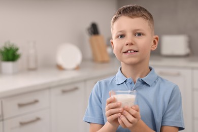 Cute boy with glass of fresh milk in kitchen, space for text