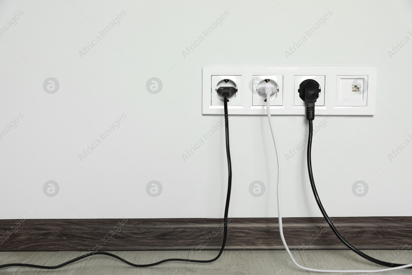 Photo of Power sockets with inserted plugs on white wall indoors, space for text. Electrical supply
