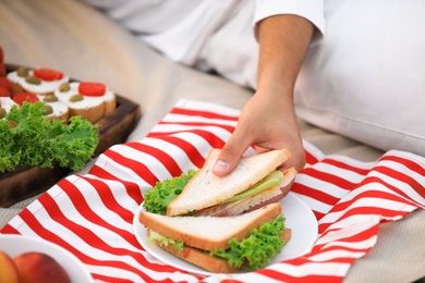 Photo of Young man with tasty sandwich lying on picnic blanket, closeup