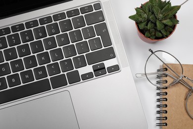 Modern laptop, houseplant, notebook and glasses on white background, flat lay